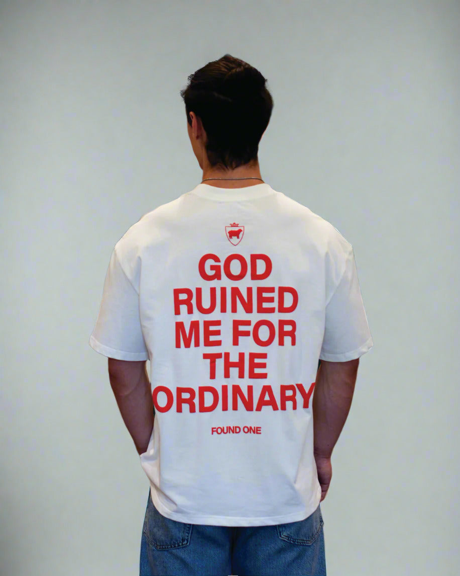 Person wearing a white t-shirt with red text in a room with green walls and decorative items.