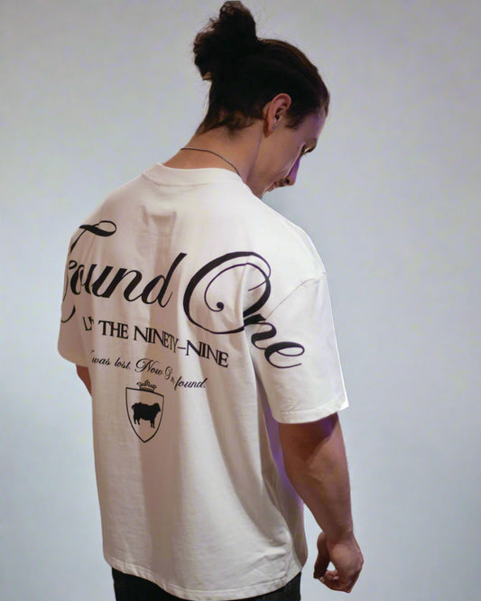 Person wearing a white t-shirt with text and graphics, standing in front of a blurred store shelf.